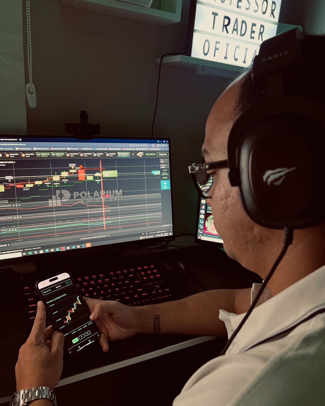 Professor Trader operando no computador com gráficos e smartphone